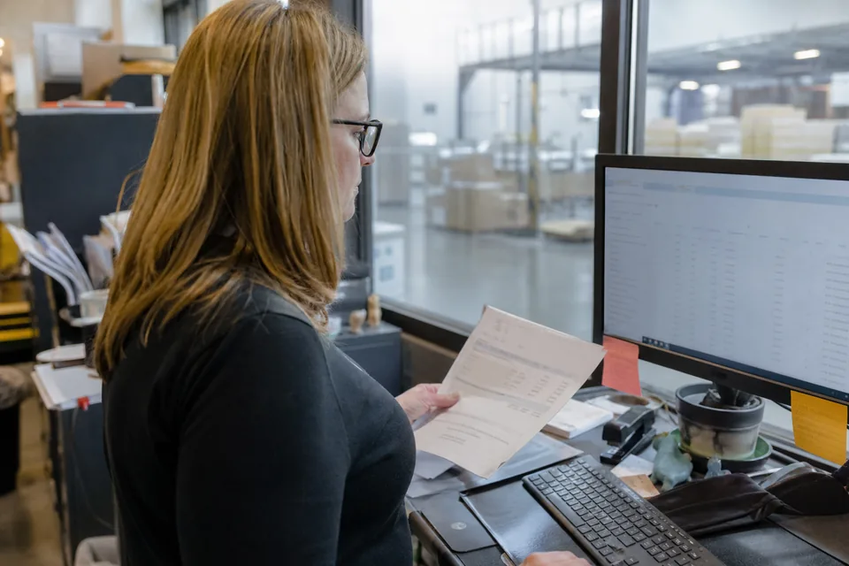 Controller at a distribution company comparing a printed bank statement with cash account transactions on a monitor