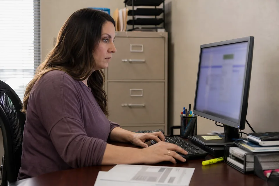 Office manager at a desktop computer with a printed bank statement and highlighter