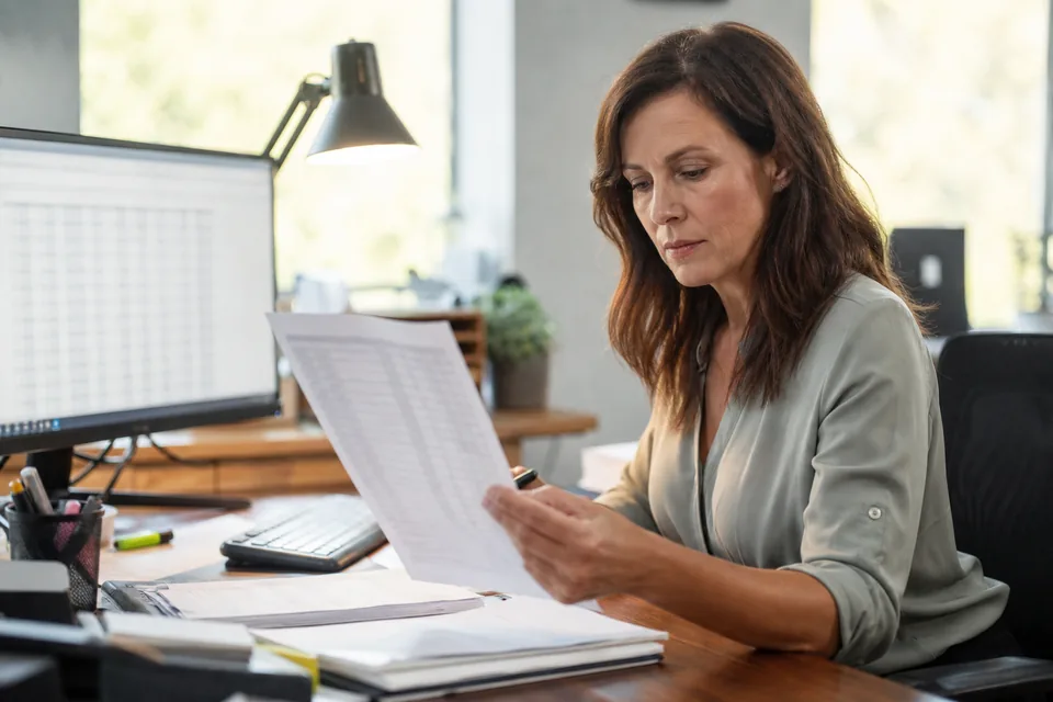 Office manager comparing a printed bank statement with the books on a desktop computer